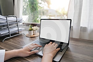 Woman hands typing on the laptop with empty blank white screen mockup. Computer is laying on the table. Person working