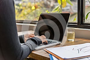 Woman hands typing laptop keyboard at workplace next to window