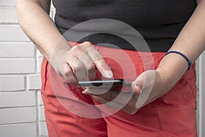 Woman hands using black mobile smart phone. White brick wall in background.