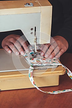 Woman hands using the sewing machine to sew a colorful face medical mask during the coronavirus pandemic. Homemade DIY