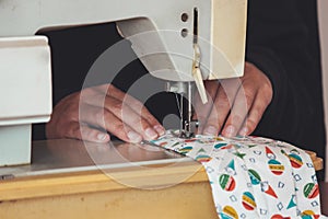 Woman hands using the sewing machine to sew a colorful face medical mask during the coronavirus pandemic. Homemade DIY protective