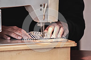 Woman hands using the sewing machine to sew the face medical mask during the coronavirus pandemic. Homemade DIY protective mask