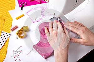 Woman hands using a sewing machine to sew a pink ladies face mask during the coronavirus pandemia. photo