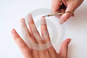 Woman hands using a small scissors to cut her fingernails on a white background. View from above. Manicure at home