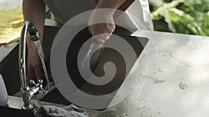 Woman hands washes foam from frying pan, under running water, metal wash basin, kitchen, summer cottage