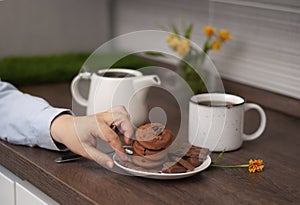 Woman hands with white kettle tea cup and choccolate cookie. Selective focus. Kitchen teatime. Time for rest and home