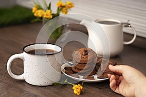 Woman hands with white kettle tea cup and choccolate cookie. Selective focus. Kitchen teatime. Time for rest and home