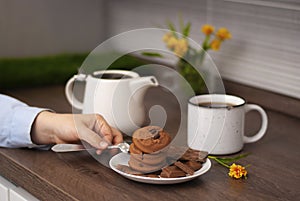 Woman hands with white kettle tea cup and choccolate cookie. Selective focus. Kitchen teatime. Time for rest and home