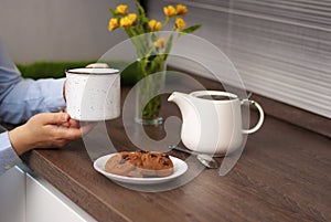 Woman hands with white kettle tea cup and choccolate cookie. Selective focus. Kitchen teatime. Time for rest and home