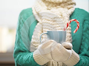 Woman hands in white woolen mittens holding a cozy cup with hot cocoa, tea or coffee. Winter and Christmas time concept.