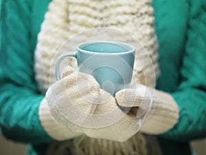 Woman hands in white woolen mittens holding a cozy cup with hot cocoa, tea or coffee. Winter and Christmas time concept.