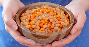 Woman hands with wooden bowl full of frozen ripe sea buckthorn berries moving it forward.