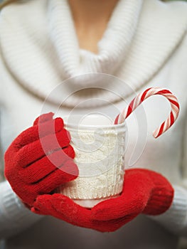 Woman hands in woolen red gloves holding a cozy mug with hot cocoa