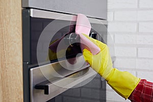 Woman hands in yellow gloves cleaning oven control panel with pink rag in kitchen.close up