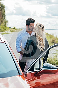 Woman and handsome man kissing and hugging near car