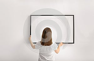 Woman hanging blank photo frame on white wall