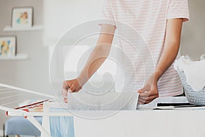 Woman hanging clean wet clothes laundry on drying rack at home laundry room