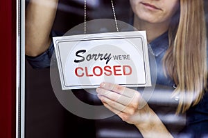 Woman hanging closed sign on small local business shop door window