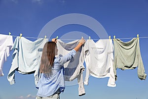 Woman hanging clothes with clothespins on washing line for drying against blue sky, back view