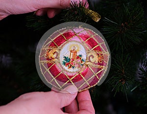 Woman hanging a cross stitched Christmas Timeless Elegance ornament on to a Christmas tree.