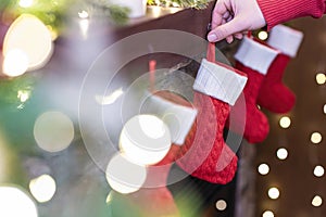 Woman hanging Ñhristmas red socks for gifts on the fireplace in bokeh lights.