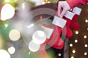 Woman hanging Ñhristmas red socks for gifts on the fireplace in bokeh lights.