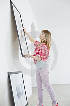 Woman hanging picture frame on wall in new house