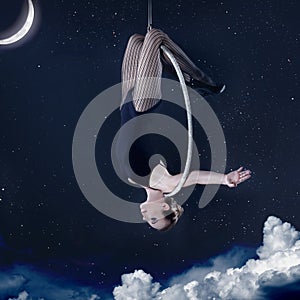 Woman hanging upside-down on aerial hoop at night