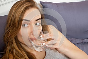 Woman hangover, woman hold glass of water lying on bed. Girl with head pain close up. young woman feel sick in the morning,