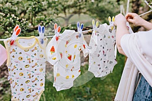 A woman hangs up baby clothes on a clothesline against the background of trees and grass bokeh