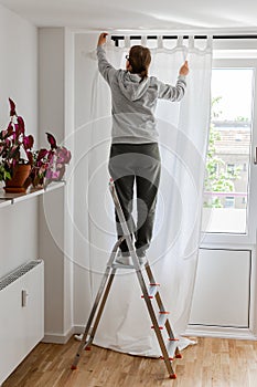 Woman hangs white curtains on the curtain rod