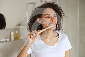 A woman happily brushes her teeth, admiring her smile in the bathroom mirror