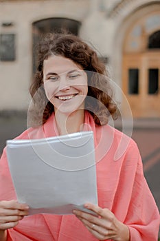 A woman happily holds securities in her hands, standing next to the university