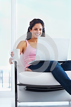 Woman, happy and coffee with laptop with reading digital blog and relax wellness in chair in home. Young person, smile