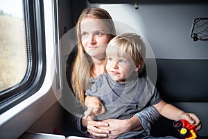 Woman with happy kid in a train compartment looks out the window. The passengers travels in the train cabin