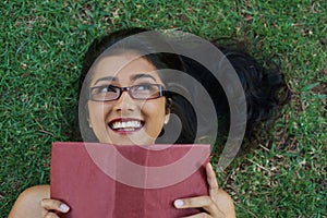 Woman, happy and reading book on grass, literature and smiling for fiction or fantasy story. Female person, nature and