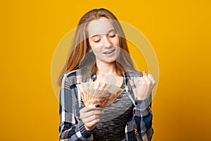 Woman, happy smiling, holding Russian rubles, wearing a plaid shirt, received a scholarship, a salary on a yellow background.