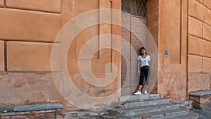 Woman in har, black pants, tshirt and sneakers holding phone in doorway