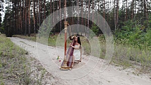 Woman harpist plays concert harp at forest sand road.