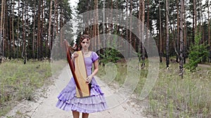 Woman harpist walks along a forest road with harp.