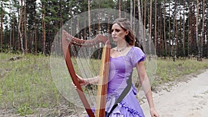 Woman harpist walks along a forest road with harp.
