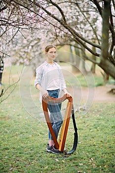 Woman harpist walks with her harp at flowering garden