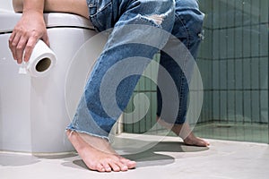 Woman has diarrhea sitting in the toilet and holding a tissue roll.