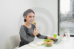 Woman has healthy business lunch in modern office interior. Young beautiful businesswoman at working place, eating vegetable