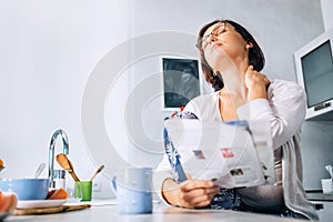 Woman has a neck pain when reads a magazine on the kitchen at mo photo