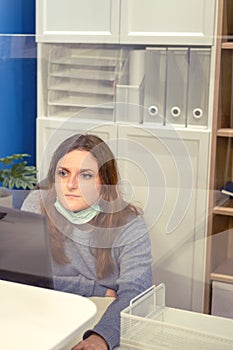 A woman has taken off her face mask and is working on a computer in a room with glass partitions. Working with coronavirus