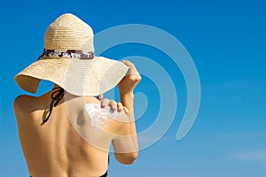 Woman in a hat applying sunscreen on her shoulder photo