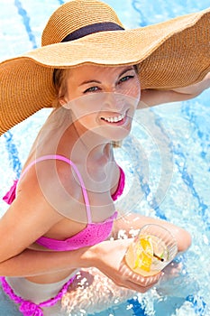 Woman in a hat enjoying cocktail in a swimming pool