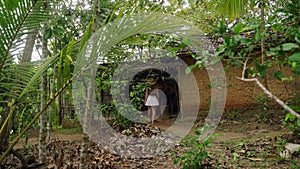 Woman in hat explores abandoned jungle hut. Adventure seeker ventures into rustic shelter amidst tropical flora