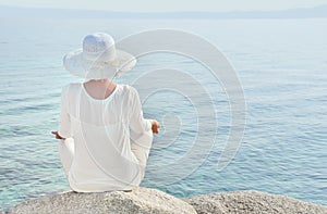 Woman with a hat facing the sea meditating